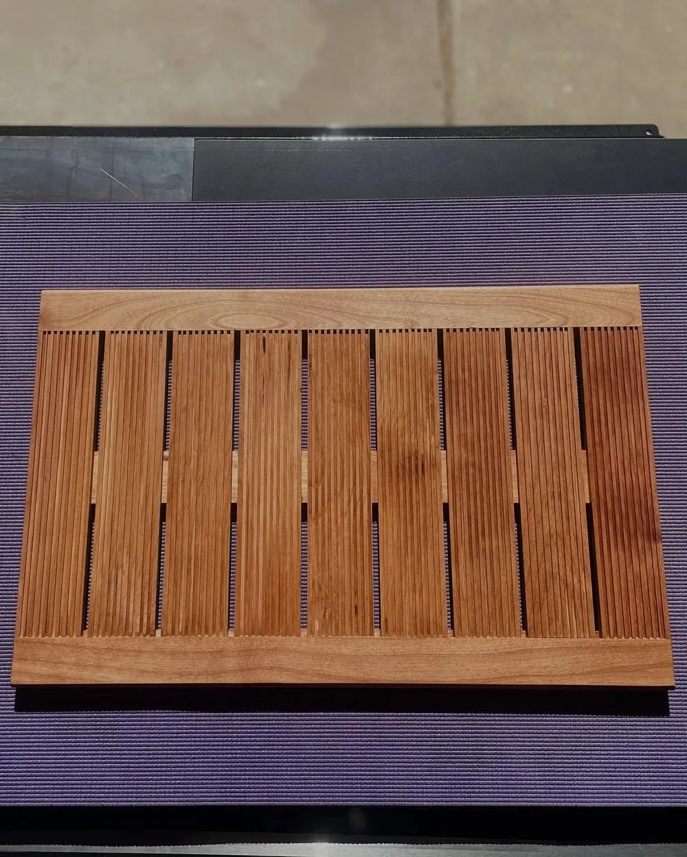 A slatted wooden bath mat photographed from directly above, its narrow strips running the length of the frame inside a solid border.
